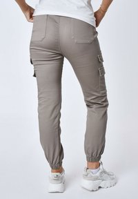 Pantaloni cargo grigi con polsini elasticizzati e molteplici tasche laterali, realizzati in un tessuto elasticizzato. Abbinati a sneakers bianche.