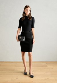 Robe noire ajustée à manches courtes et finition texturée, associée à une jupe crayon taille haute avec des accents de boutons et un petit sac à main noir.
