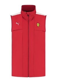 Czerwona bezrękawnik wykonany z lekkiego materiału, z wysokim kołnierzem, zamkiem błyskawicznym z przodu, białymi akcentami i logo Ferrari po lewej stronie klatki piersiowej.