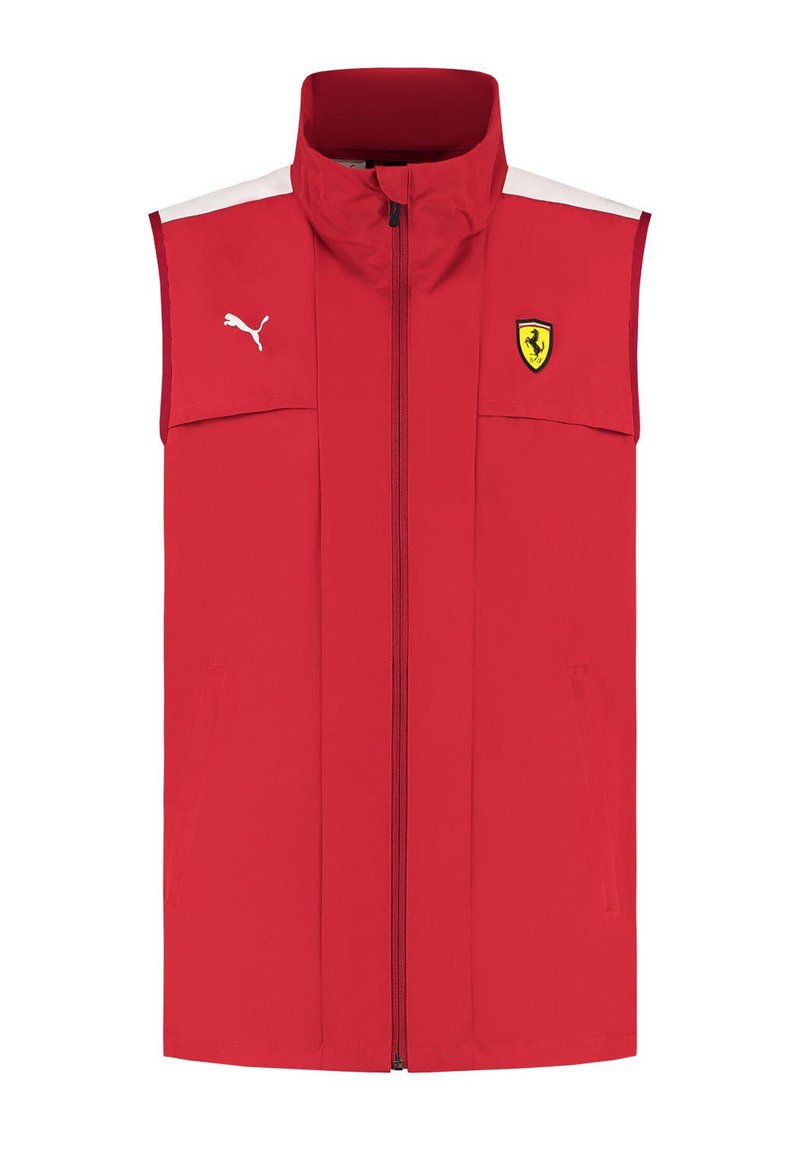 Czerwona bezrękawnik wykonany z lekkiego materiału, z wysokim kołnierzem, zamkiem błyskawicznym z przodu, białymi akcentami i logo Ferrari po lewej stronie klatki piersiowej.