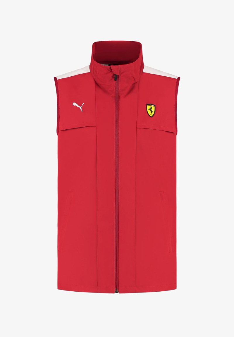 Czerwona bezrękawnik wykonany z lekkiego materiału, z wysokim kołnierzem, zamkiem błyskawicznym z przodu, białymi akcentami i logo Ferrari po lewej stronie klatki piersiowej.
