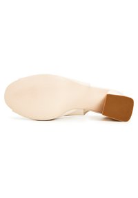 Vaaleanbeige korkokenkä, jossa on sileä päällinen, neliskanttinen varvas ja ruskea kumipohja. Teksturoitu ulkopohja, jossa on hienovaraisia uurteita pidon lisäämiseksi.