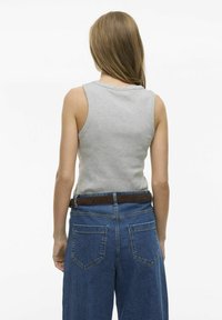 Grå ärmlös topp i kombination med högmidjade blå denimjeans med ett brunt bälte. Fokusera på bakvy och enkel, avslappnad design.