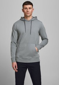 Sudadera gris con capucha, con cordones ajustables, bolsillo frontal y puños acanalados. Fabricada con una tela suave y de textura lisa.