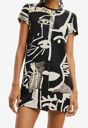 Robe noire et blanche en coton, présentant des motifs de visages abstraits avec des lignes audacieuses et des textures contrastées, manches courtes et coupe décontractée.