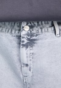 Lichtgrijze spijkerbroek van denim met een vervaagd patroon, voorzien van een zilveren knoop, gestikte tailleband en subtiele kleurvariaties.