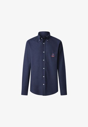 Granatowa koszula z długim rękawem zapinana na guziki, z kołnierzykiem zapinanym na guziki i małym haftowanym herbem po lewej stronie klatki piersiowej.