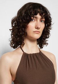 Top castanho com decote halter, com detalhes franzidos na linha do pescoço, feito de um tecido suave. Apresenta um design sem mangas e uma silhueta ajustada.
