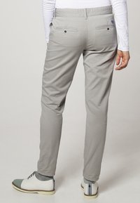 Světle šedé kalhoty z bavlny s úzkým střihem, obsahující dvě zadní kapsy se zapínáním na knoflíky a jednotnou texturou. Pár bílých bot s zelenými akcenty.