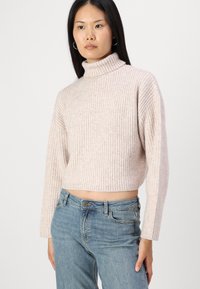 Helle rosa gerippte Rollkragensweatshirt mit langen Ärmeln und cropped Schnitt, kombiniert mit blauen, hoch taillierten Jeans.