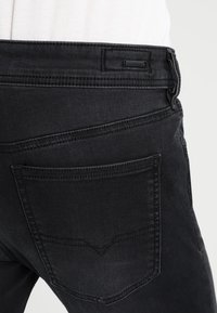 Svarta jeans i denim med detaljerade bakfickor, synlig sömnad och en etikett. Har en slät textur och en figurnära design.