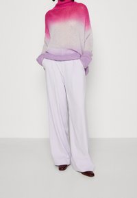 Pull en tricot à col roulé avec dégradé de rose à lavande, associé à un pantalon taille haute lavande, avec jambes larges et plis subtils.