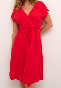 Robe rouge à manches courtes, décolleté en V et taille nouée. Le tissu semble lisse, créant une silhouette fluide.