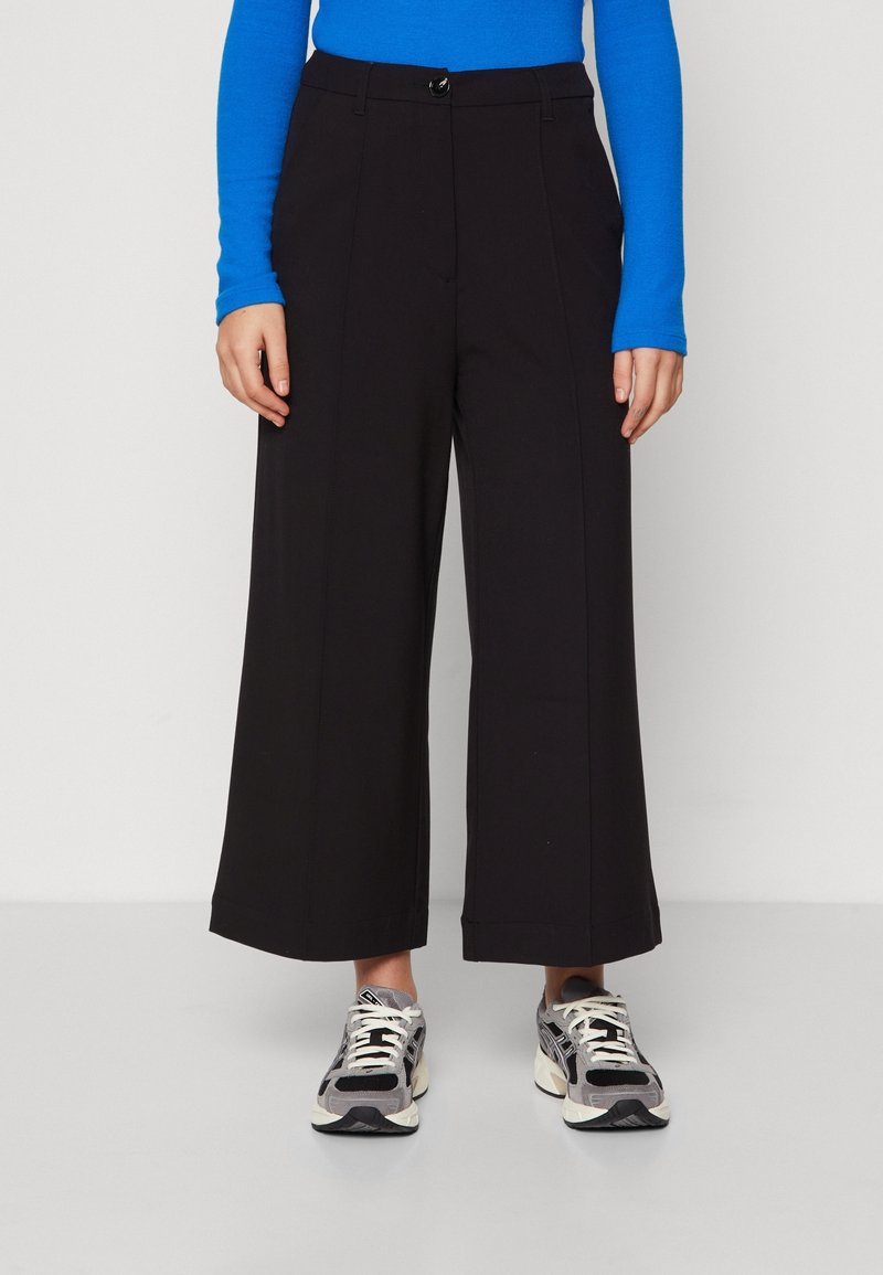 Svarta vida byxor med hög midja, som har en knappstängning och framfickor. Kombinationen med grå och svarta sneakers.