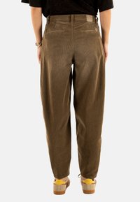 Pantaloni in velluto a coste di colore verde oliva, con vestibilità comoda, due tasche posteriori e una superficie texturizzata. Abbinati a calzature di supporto.