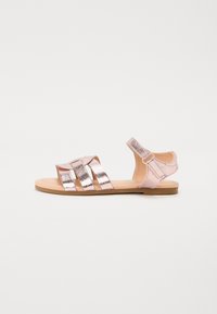 Rosa sandal med metallisk remdesign, platt sula, öppen tå och ankelrem. Har tre breda horisontella remmar på ovansidan.