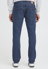 Tamnoplave traperice ravnog kroja s dva zakrpljena stražnja džepa i kožnom oznakom s markom na pojasu.