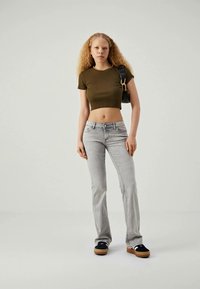 Jean évasé gris, haut court vert et chaussures à plateforme noires. La tenue présente un design ajusté avec une texture unie et un minimum de détails.