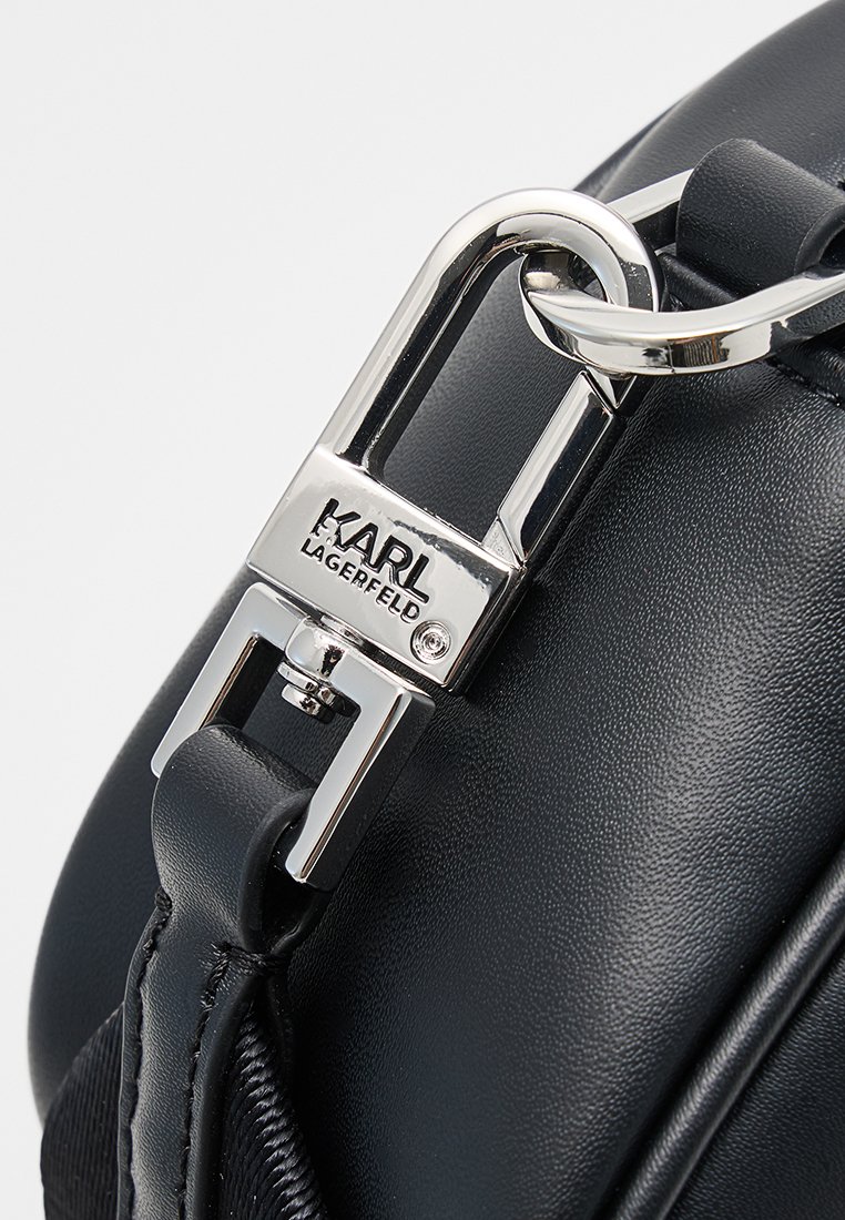 Bolso de cuero negro con un cierre de metal plateado con el logo "KARL LAGERFELD", textura suave y una sujeción de correa resistente.
