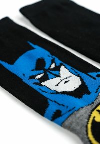 Calzini neri con una grafica blu e bianca che rappresenta il volto di un personaggio mascherato. Realizzati in tessuto lavorato a maglia con una superficie liscia.