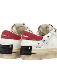 Sneakers bianchi con accenti rossi e neri, in pelle testurizzata e con una finitura vissuta. Presentano dettagli con il marchio e borchie metalliche sui lati.