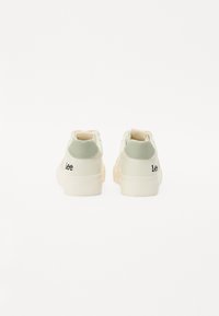 Zapatillas blancas con un suave tirador de talón verde y detalle del logo en negro. Acabado suave con acentos cosidos, diseño de corte bajo y suela de goma.
