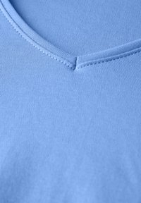 Světle modré tričko s výstřihem do V vyrobené z měkké, žebrované bavlny. Obsahuje pečlivé švy podél výstřihu a hladkou, jednotnou texturu.