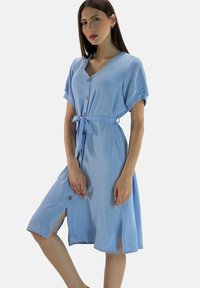 Abito camicia azzurro chiaro con maniche corte, cinturino in vita, tessuto testurizzato e spacchi laterali; presenta bottoni in legno naturale.