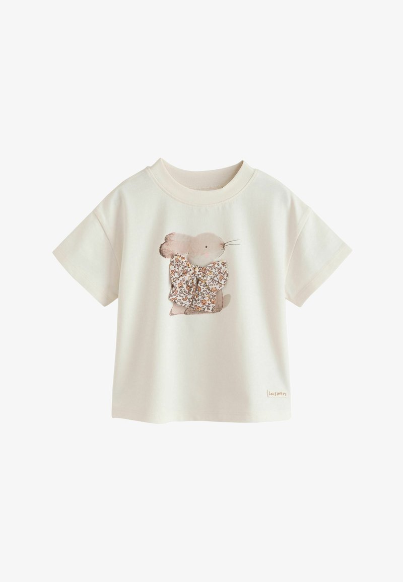 Camiseta de manga corta color crema con un ratón estampado que lleva un gran lazo floral en la parte delantera.
