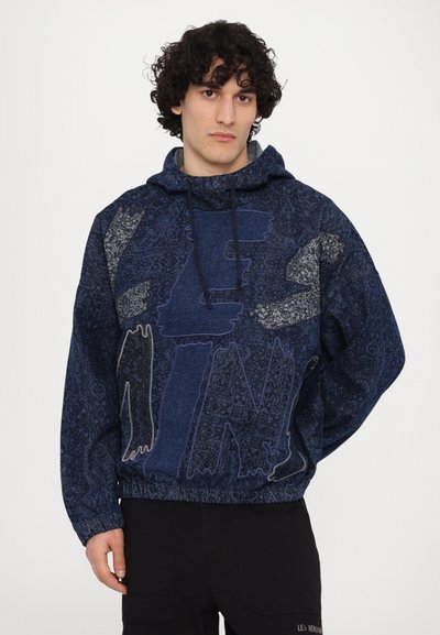 Haut de survêtement à capuche bleu marine avec un design à motifs, cordon de serrage et poignets élastiques. Présente de grandes lettres en gras dans des couleurs contrastées.