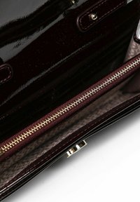 Bolso burdeos brillante con un compartimento con cremallera, que cuenta con un interior beige con un patrón sutil y detalles metálicos.