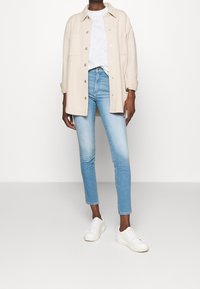 Beige skjortjacka, vit t-shirt, ljusblå skinny jeans och vita sneakers. Mjuk tyg och åtsittande design.