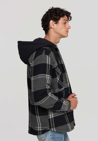 Koszula w kratę z flaneli w odcieniach szaro-czarnych, z czarnym kapturem, zapięciem na guziki i długimi rękawami. Teksturowana tkanina w luźnym kroju.