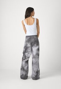 Hvit ermeløs tank topp med svarte nagler langs halslinjen, kombinert med løse, grå tie-dye cargo bukser med sidelommer.