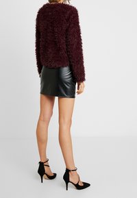 Burgundské umělé kožešinové sako s dlouhými rukávy; v kombinaci s přiléhavou černou koženou minisukní a černými lodičkami na vysokém podpatku.