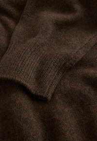 Barna kötött pulóver anyaga bordás mandzsettával, puha textúrával és meleg, gazdag színnel. A minta egységes és sűrű.