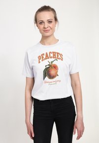 Bílé tričko s grafikou dvou broskví s zelenými listy. Nápis "PEACHES" je výrazný a oranžový, pod ním text "Delicious and juicy".