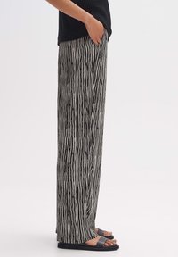 Zwart-wit gestreepte wijde broek van lichtgewicht stof, met een losse pasvorm en zakken. Gecombineerd met platte zwarte sandalen.