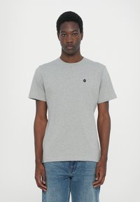 Tricou gri cu mânecă scurtă, din bumbac, cu guler rotund și un mic logo negru pe partea stângă a pieptului. Croială clasică și textură.