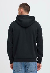 Svart hettegenser med hette, ribbestrikkede mansjetter og kant; myk tekstur; brukt sammen med lyseblå jeans, som viser et uformelt design.