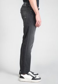 Jeans de mezclilla gris con corte recto, que cuentan con cinco bolsillos y detalles de costura sutiles, combinados con zapatillas en blanco y negro.