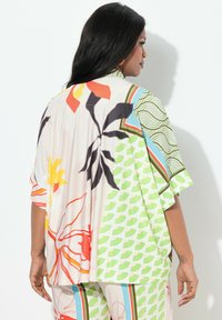 Luftig blomstret bluse lavet af letvægtigt stof, med levende farver som grøn, orange og rød, samt et abstrakt geometrisk mønster.