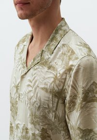 Korte mouwen, knoopsluiting shirt in lichtbeige met een gestructureerde afwerking, met een tropisch bladerenpatroon in gedempte groentinten.