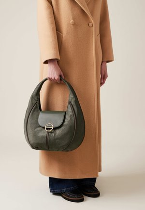 Green textured handbag with a curved shape, featuring a flap and circular hardware detail, held by a person in a beige coat.