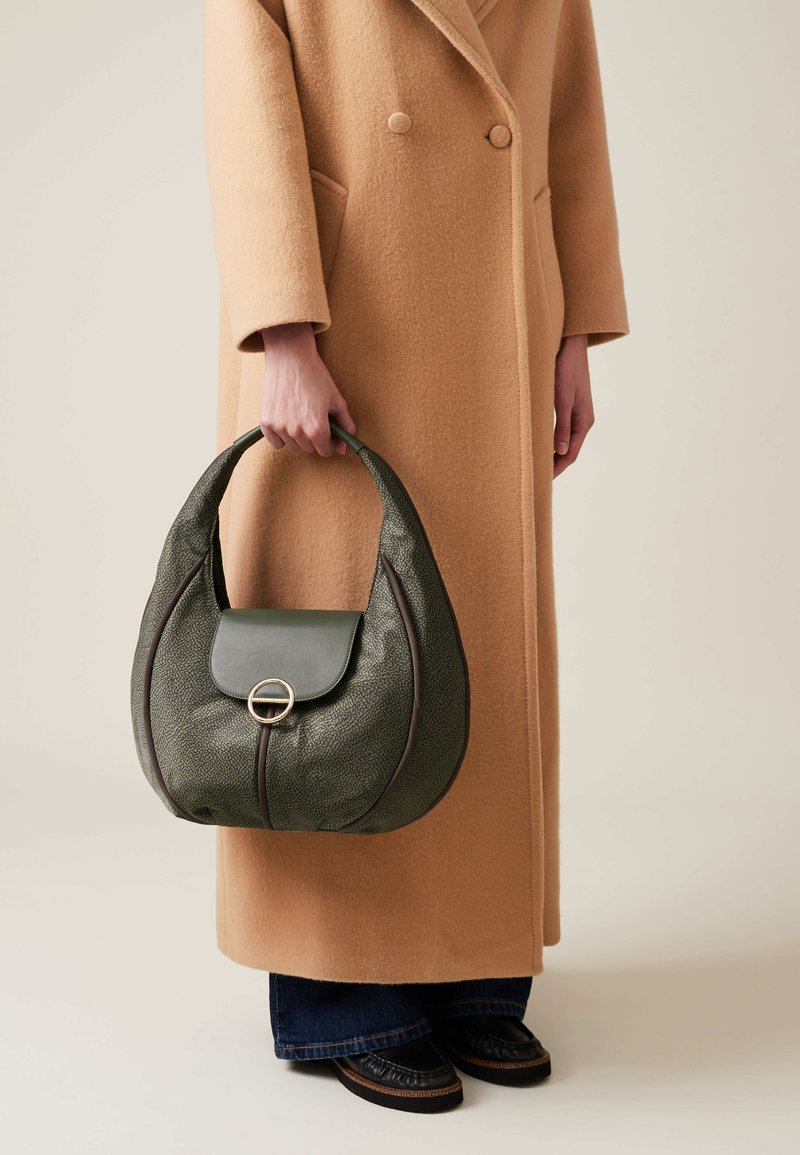 Green textured handbag with a curved shape, featuring a flap and circular hardware detail, held by a person in a beige coat.