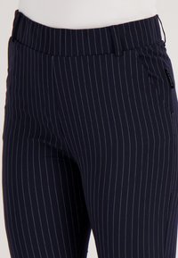 Navyblauwe broek met dunne verticale witte strepen, getailleerde taille en zijzakken, gedragen met een wit topje.