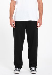 Zwarte, loszittende broek van katoen met een rechte pijp. Gecombineerd met een wit shirt en zwarte sneakers.