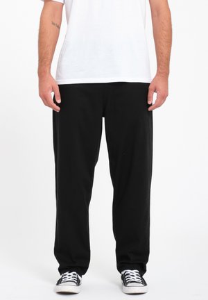 Pantalones negros de corte amplio en tejido de algodón, con un diseño de pierna recta. Combinados con una camisa blanca y zapatillas negras.