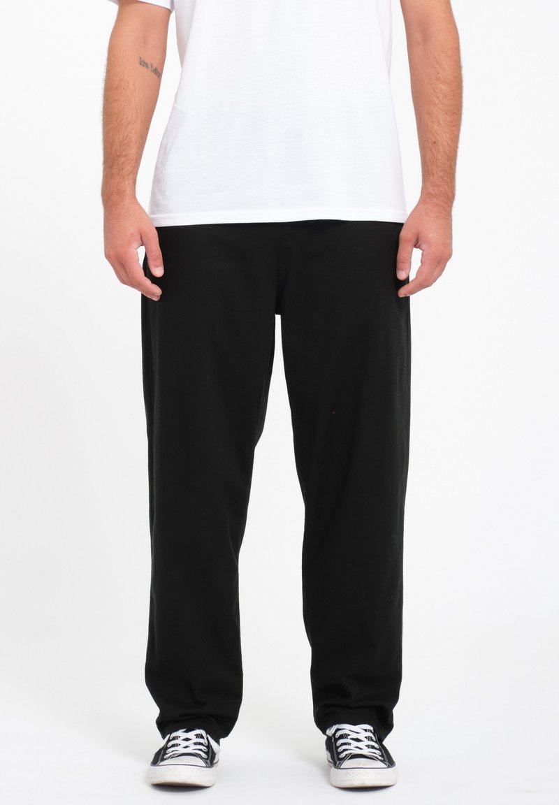 Zwarte, loszittende broek van katoen met een rechte pijp. Gecombineerd met een wit shirt en zwarte sneakers.