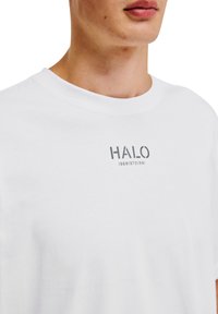 Hvid bomulds T-shirt med rund halsudskæring og korte ærmer, med teksten "HALO 196819721981" trykt i grå på brystet.